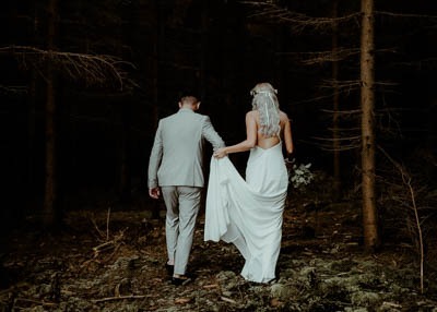 Svadobný fotograf zachytil mladomanželov, ako šťastne kráčajú ruka v ruke cez slnkom zaliaty les.